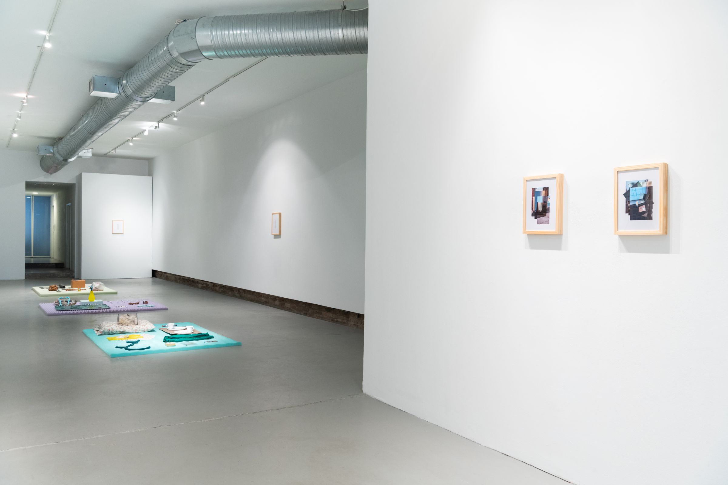 White-walled gallery showing two framed images on the wall in the foreground and floor sculptures in the background