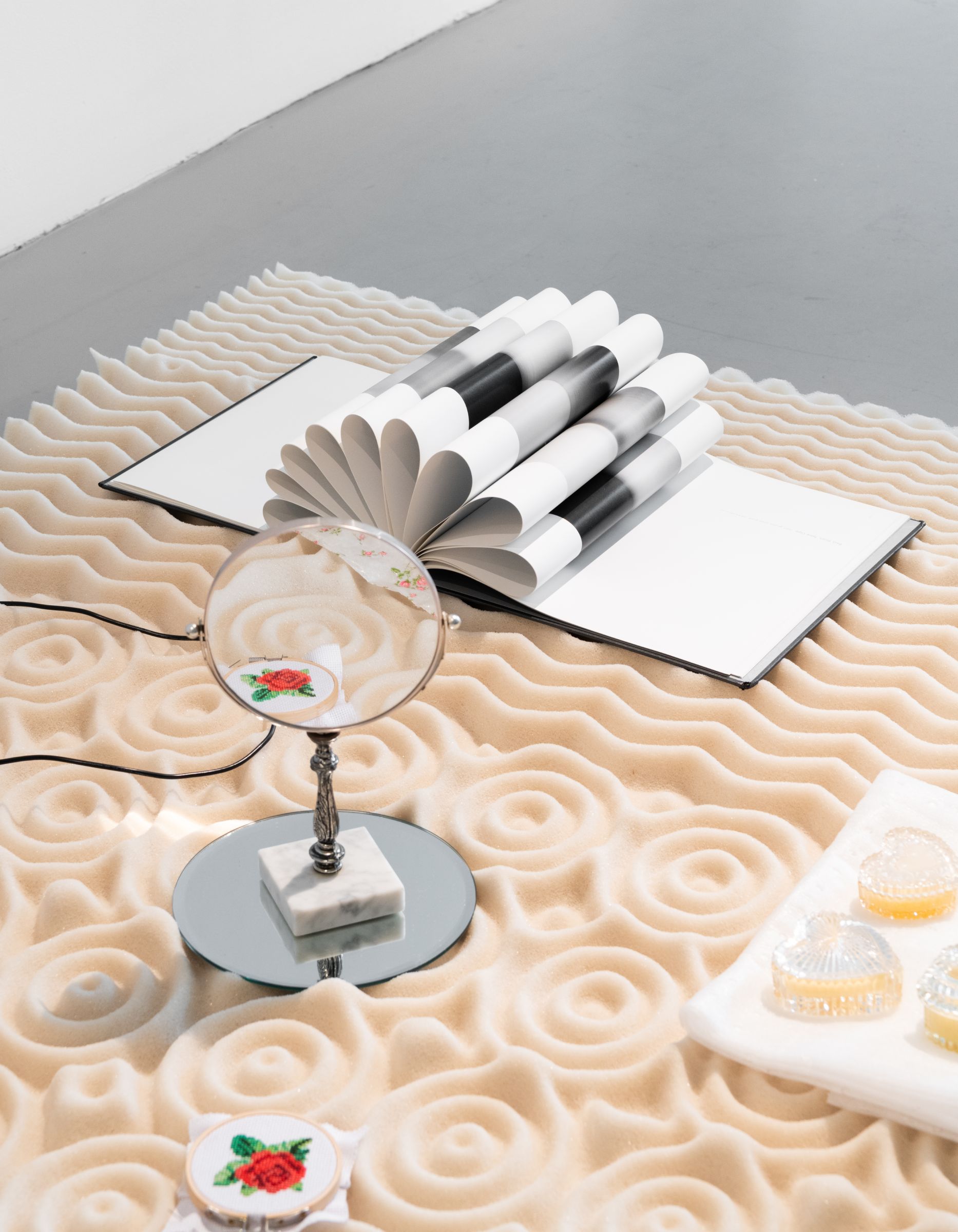 A textured tan mattress topper on the floor with a mirror and pages of a book splayed open 