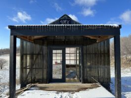 Entrance to a greenhouse with a porch with snow on the ground and blue skies above