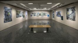 Wooden bench facing a wall in a gallery displaying abstract blue, white and black artworks