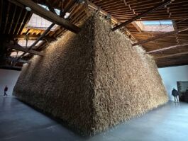 Large brown structure made of mud and dried grass inside of an industrial space