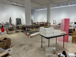 Large industrial space filled with tables and boxes and objects meant for an art exhibition