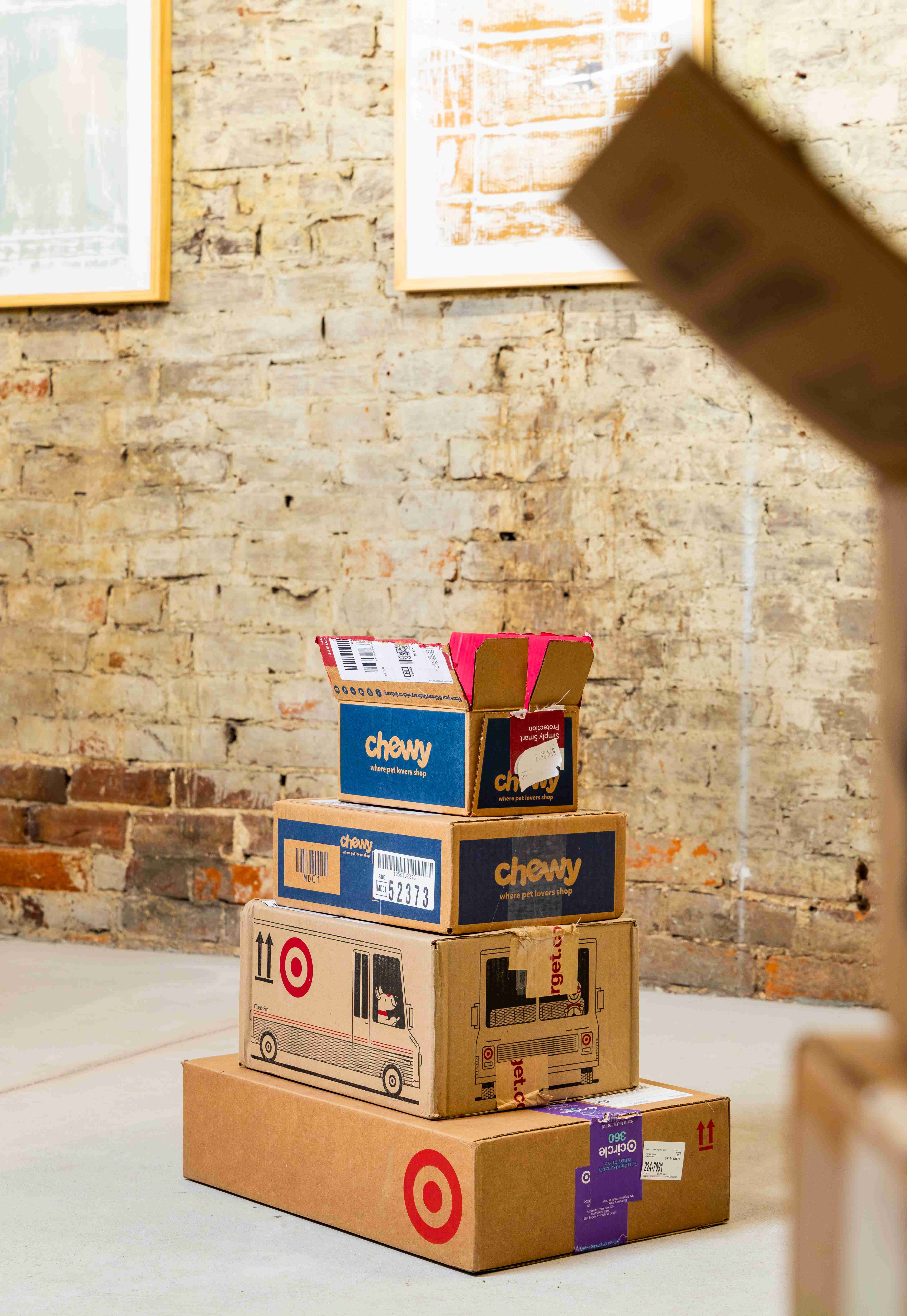 Stack of cardboard boxes sitting on the floor in front of an exposed brick wall with another stack of cardboard boxes in the foreground 