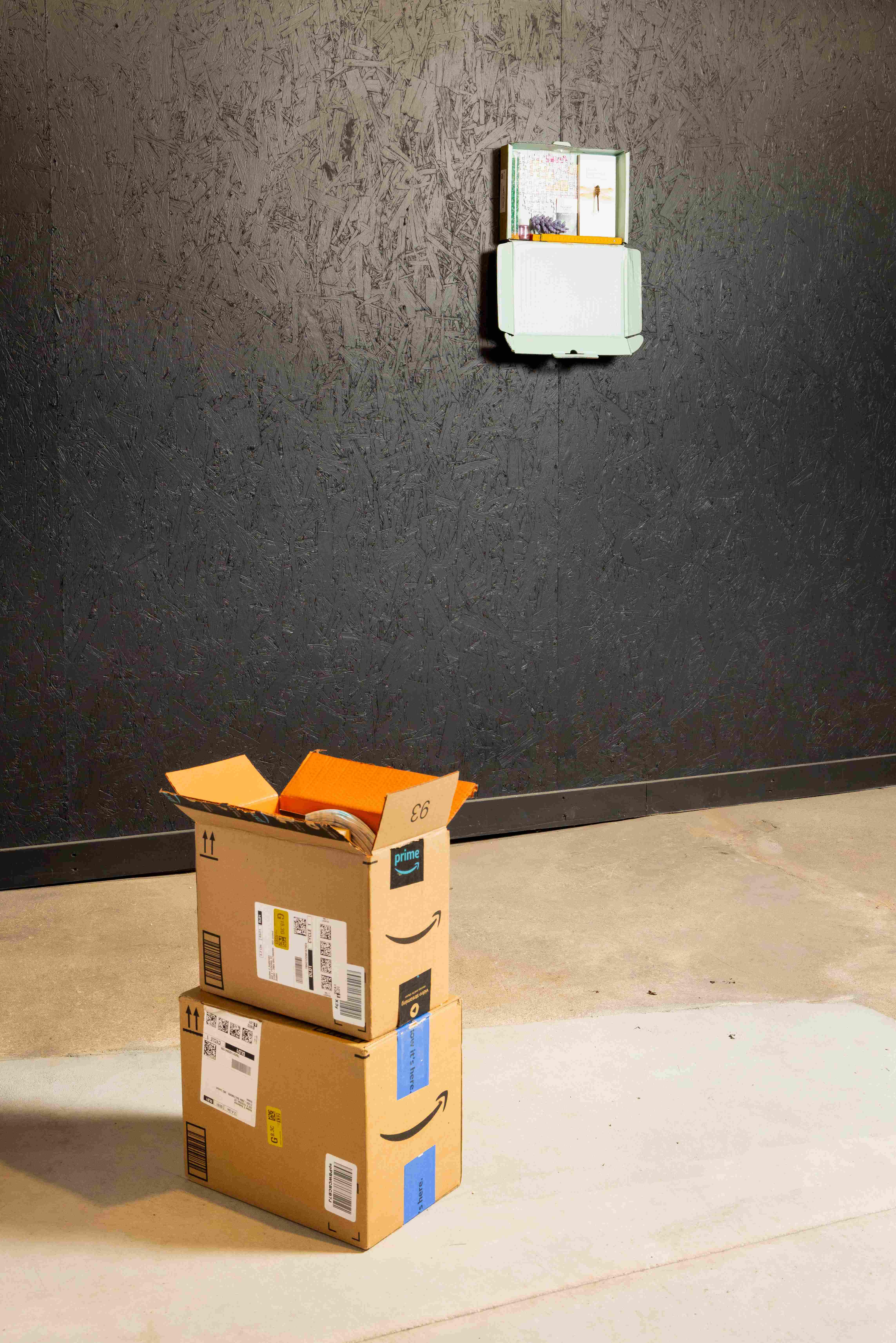 Two boxes sitting on the floor in front of a black wall with a light blue object on it